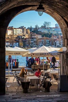 people are sitting at tables under umbrellas near the water with buildings in the background