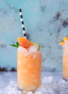 two glasses filled with orange juice and garnished with limes on top of ice