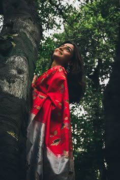 a woman standing next to a tree wearing a red and white dress with leaves on it