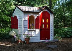 a little red and white house in the middle of a forest with potted plants