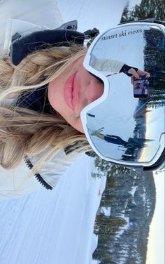 a woman wearing ski goggles standing in front of a snow covered field with trees