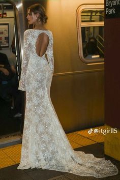 a woman in a white dress standing on a subway platform with her back to the camera