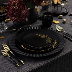 a black and gold table setting with plates, silverware and flowers in vases