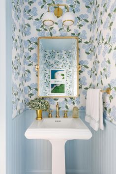 a bathroom with blue and white wallpaper, gold faucet, sink and mirror