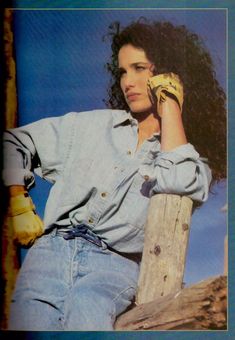 a woman leaning on a wooden fence with a banana in her hand and wearing jeans