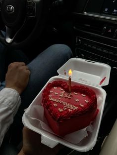 a heart shaped cake with a lit candle in the shape of a heart is being held by a man