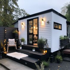 a tiny house with lights on the porch and steps leading up to it's front door