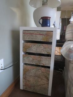 a white cabinet with three drawers and a map on it's front, next to a lamp