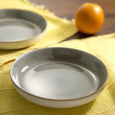 two white bowls sitting on top of a yellow table cloth next to an orange slice