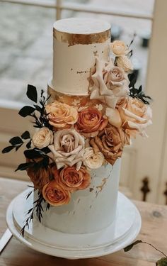 a white and gold wedding cake with flowers on the top is sitting on a table