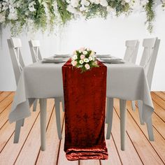 the table is set with white and red flowers on it, along with silver chairs