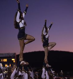 two cheerleaders doing tricks in front of a crowd at a football game with the lights on