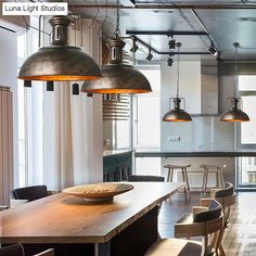 an industrial style kitchen and dining room with wooden table, pendant lights over the island