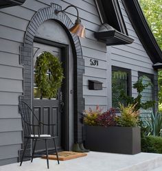 the front door of a gray house with a wreath on it and two chairs outside