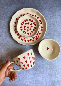 a hand holding a coffee cup and saucer with hearts painted on the cups in red