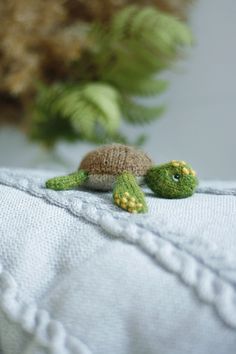 two tiny turtle figurines sitting on top of a white blanket next to green plants