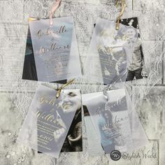 four wedding cards hanging from strings on a lace covered tablecloth with gold foil lettering