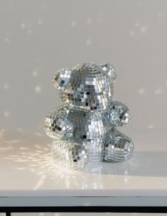 a silver teddy bear sitting on top of a white table next to a mirror ball