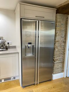 a stainless steel refrigerator in a kitchen with white cabinets and wood flooring next to a stone wall