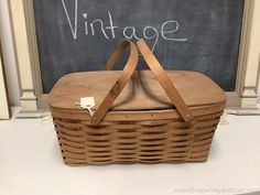 a wicker picnic basket sitting in front of a chalkboard with the word vintage written on it