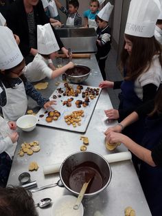 children in chef's hats and aprons making cookies on a table with pans