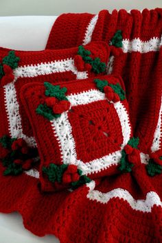 two crocheted red and white christmas blankets with holly decorations on them, sitting on a couch