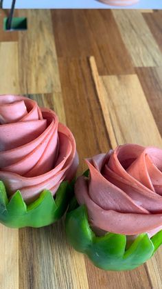 two cupcakes with pink frosting and green leaves on a wooden table top