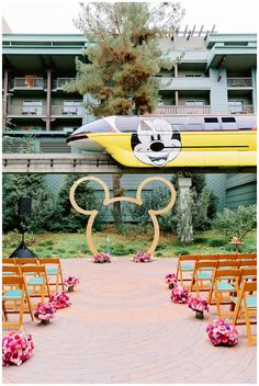 an outdoor ceremony area with chairs and mickey mouse head on the aisle, decorated with pink flowers