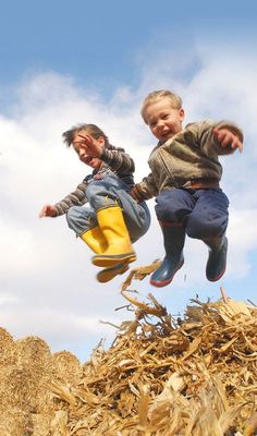 two young boys jumping in the air on top of a pile of wood and corn