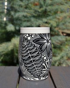 a black and white coffee cup sitting on top of a wooden table next to trees