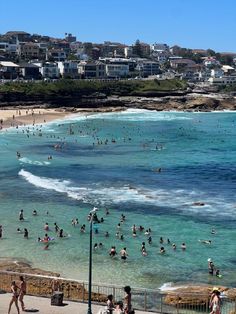 many people are swimming in the ocean near some buildings and beach goers on a sunny day