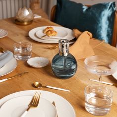 a wooden table topped with white plates and silverware