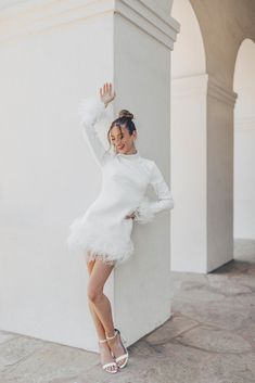 a woman in a white dress is leaning against a pillar and posing for the camera