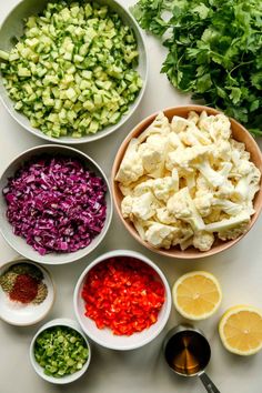 bowls filled with different types of vegetables on top of a white table next to lemons and parsley