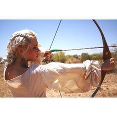 a woman with blonde hair is aiming an arrow at something in the air while wearing a white dress