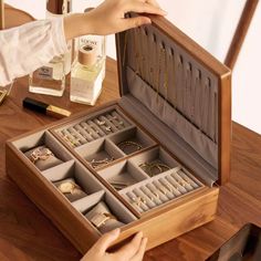 an open wooden jewelry box on a table next to a woman's hand holding it