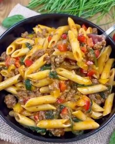 a black bowl filled with pasta and meat on top of a table next to vegetables