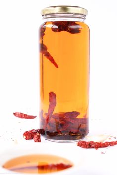 a glass jar filled with liquid and dried red chili peppers on the ground next to it