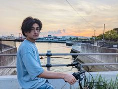 a young man sitting on top of a bike next to the ocean at sunset or dawn