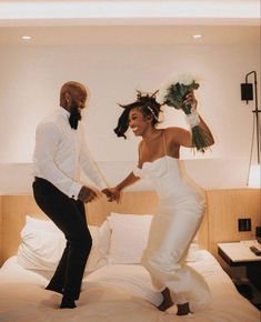 a man and woman are dancing on the bed in their hotel room, holding hands