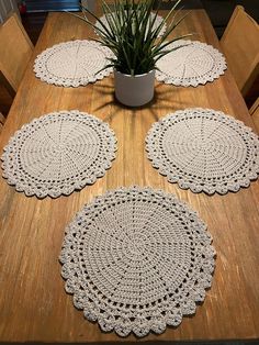 four crocheted placemats sitting on top of a wooden table next to a potted plant