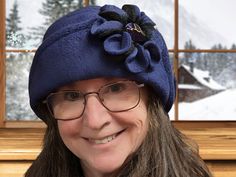 a woman wearing glasses and a blue hat with a flower on the top is smiling at the camera