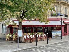 an empty street with tables and chairs in front of a restaurant on the sidewalk near a tree