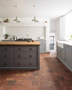 a kitchen with grey cabinets and wooden counter tops, an island in the middle is surrounded by hanging lights