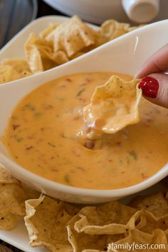 a person dipping tortilla chips into a white bowl filled with cheese and salsa