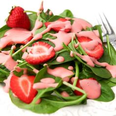 a white plate topped with spinach covered in pink icing and strawberries next to a fork