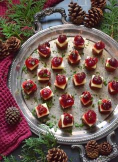 small desserts are arranged on a silver platter with pine cones and greenery