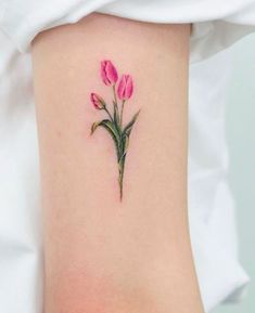 a small pink flower tattoo on the right side of the arm, with green stems growing out of it