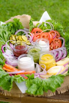 a basket filled with lots of vegetables and sauces on top of green grass next to a wooden table