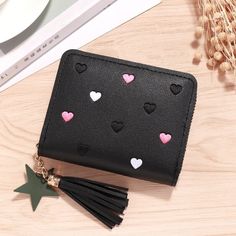 a black wallet with hearts and tassels on the front is sitting on a table